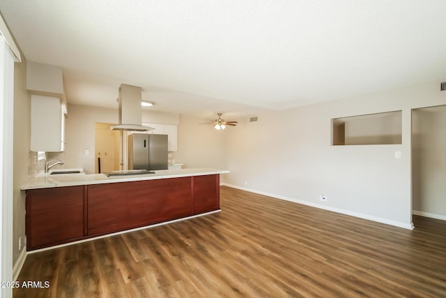 kitchen featuring stainless steel fridge, a peninsula, island exhaust hood, light countertops, and a sink