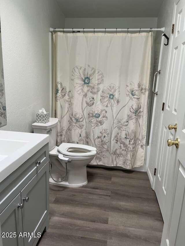 bathroom featuring a textured wall, toilet, wood finished floors, vanity, and a shower with curtain