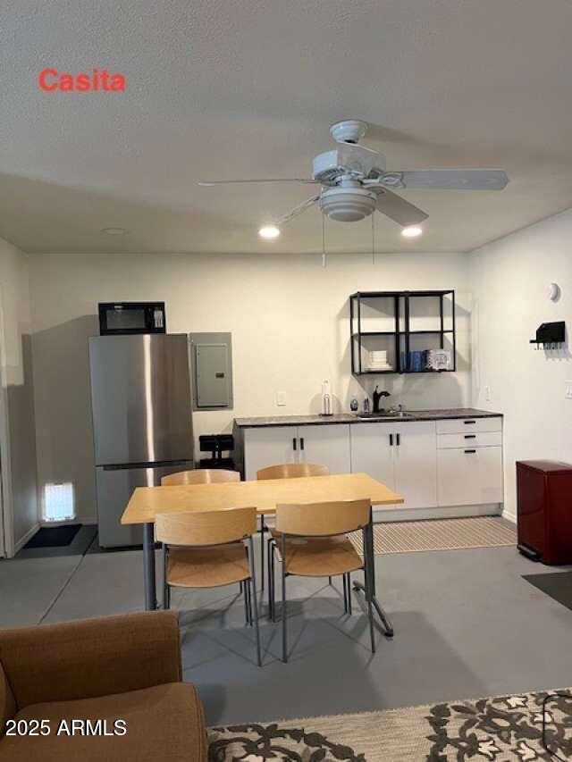 kitchen featuring black microwave, electric panel, ceiling fan, freestanding refrigerator, and white cabinetry