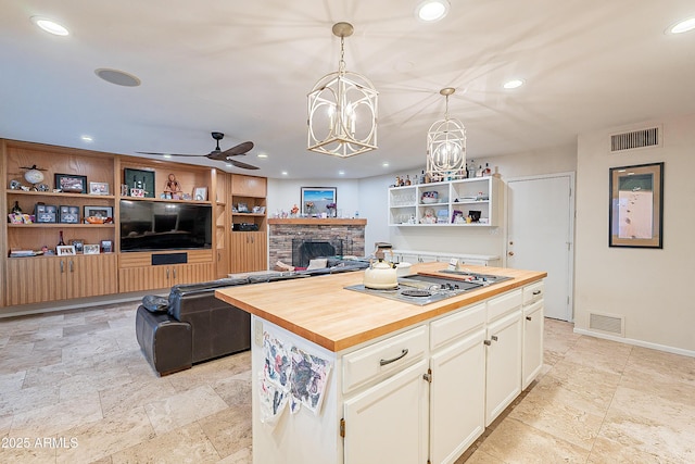 kitchen featuring a kitchen island, a fireplace, decorative light fixtures, wooden counters, and stainless steel gas cooktop