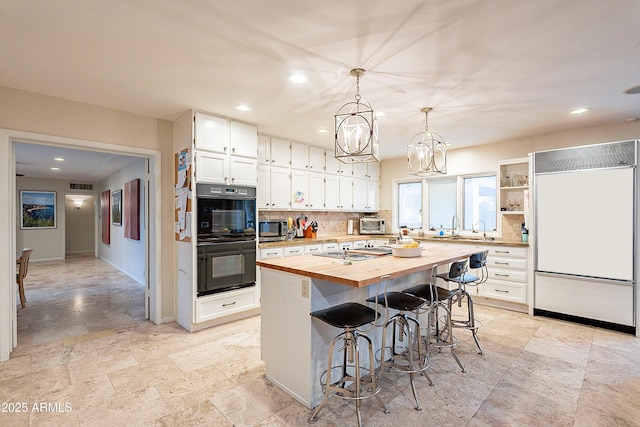 kitchen with butcher block countertops, double oven, paneled fridge, a kitchen island, and white cabinets