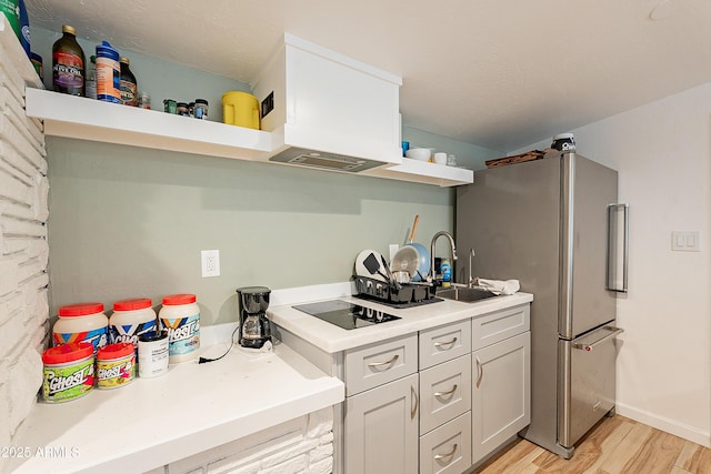 kitchen featuring sink, black electric stovetop, stainless steel fridge, and light hardwood / wood-style floors