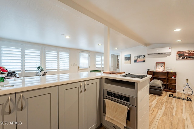 kitchen with light hardwood / wood-style flooring, a wall mounted air conditioner, oven, and kitchen peninsula