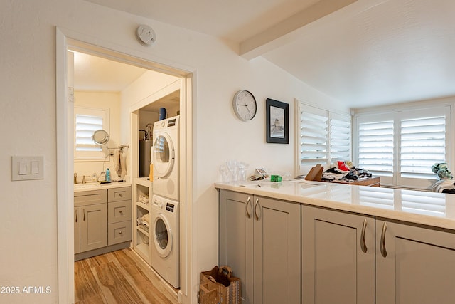 laundry room featuring stacked washer and dryer, plenty of natural light, sink, and light wood-type flooring