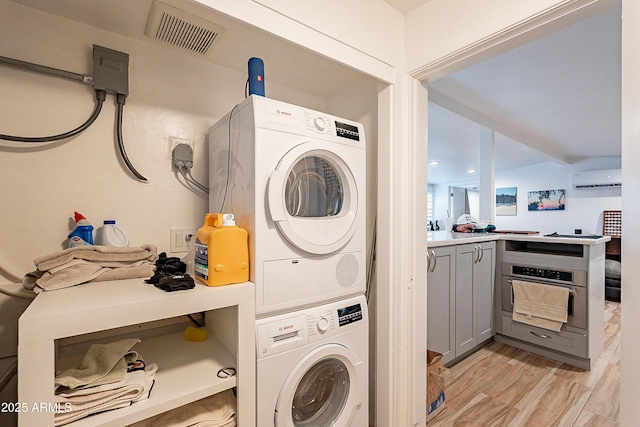 clothes washing area with light hardwood / wood-style flooring, a wall mounted AC, and stacked washer / dryer