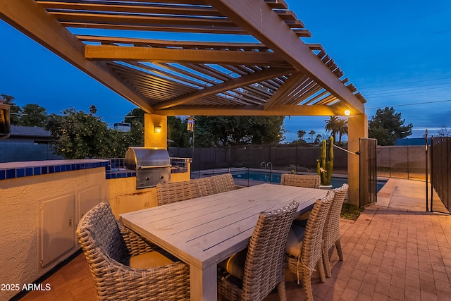 patio terrace at dusk featuring a pergola, grilling area, and an outdoor kitchen