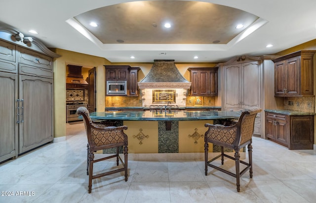 kitchen with a tray ceiling, a center island, custom range hood, and appliances with stainless steel finishes