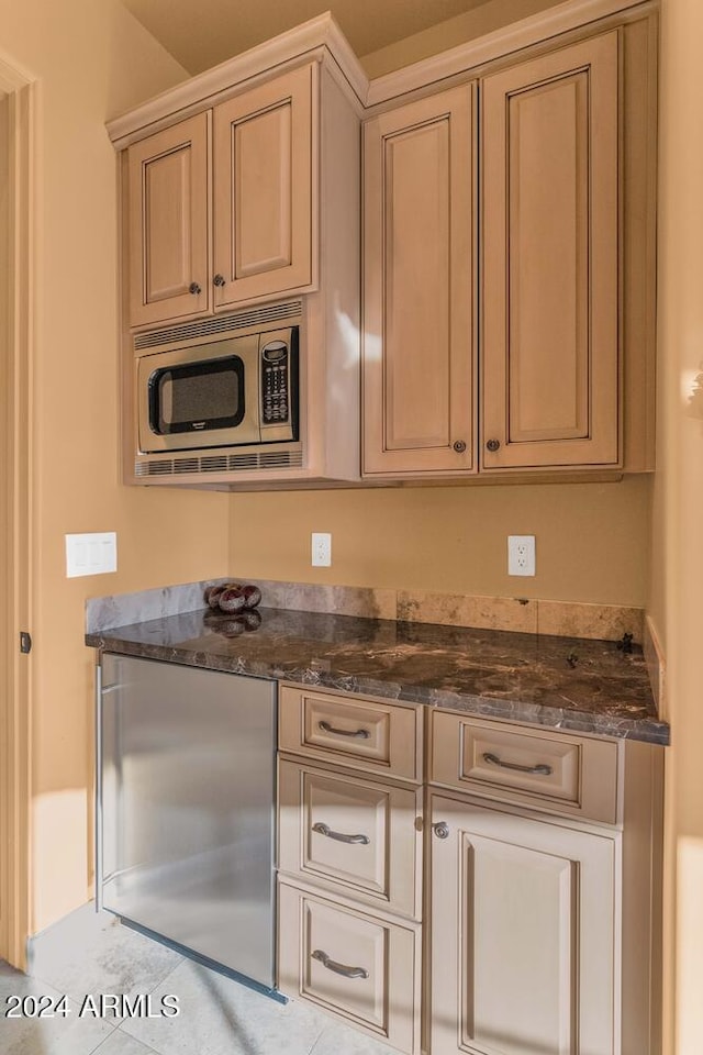 kitchen with light tile patterned flooring, dark stone countertops, and stainless steel appliances