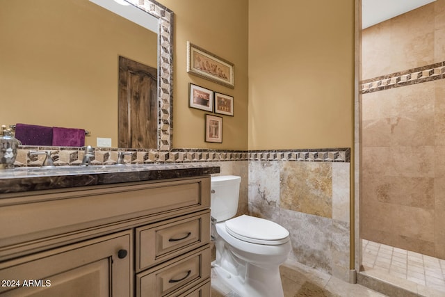 bathroom featuring vanity, tile patterned flooring, toilet, tiled shower, and tile walls