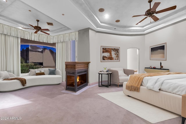 carpeted bedroom with a raised ceiling and ceiling fan