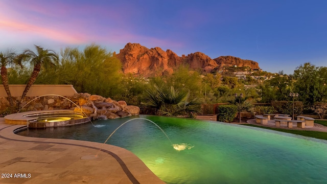 pool at dusk featuring pool water feature and an in ground hot tub