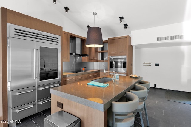 4800 N 68th St Unit 101, Scottsdale, AZ 85251 - kitchen featuring stainless steel appliances, a sink, wall chimney range hood, brown cabinetry, and dark tile patterned floors