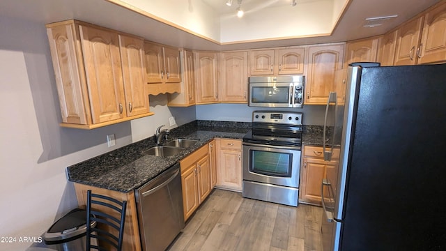 kitchen with sink, dark stone counters, light hardwood / wood-style flooring, stainless steel appliances, and a tray ceiling