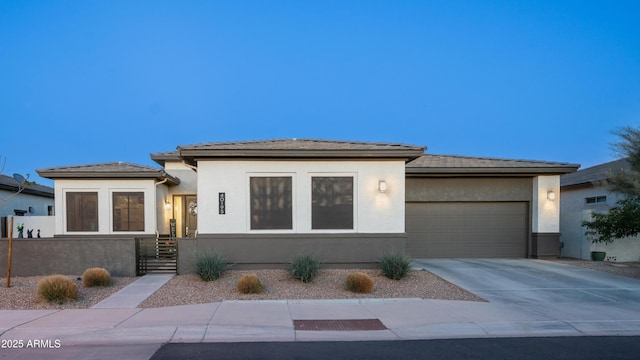 prairie-style home with concrete driveway, an attached garage, a tile roof, and stucco siding