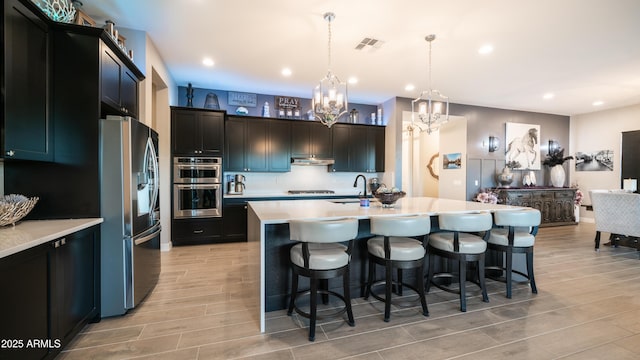 kitchen featuring a breakfast bar, wood finish floors, stainless steel appliances, light countertops, and visible vents