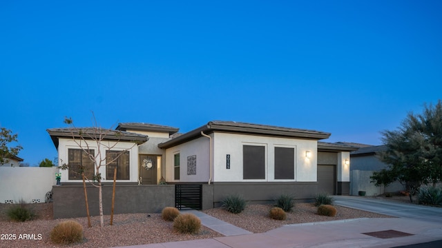 prairie-style house with driveway, a fenced front yard, an attached garage, and stucco siding