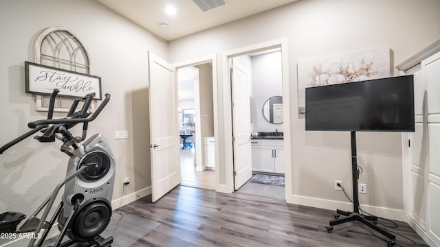 workout area with visible vents, a sink, baseboards, and wood finished floors