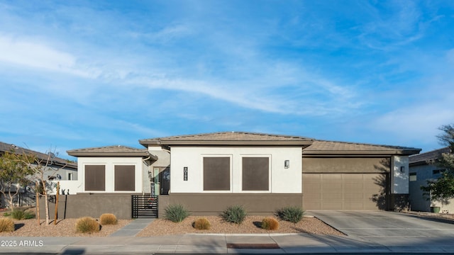 prairie-style home with concrete driveway, an attached garage, and stucco siding