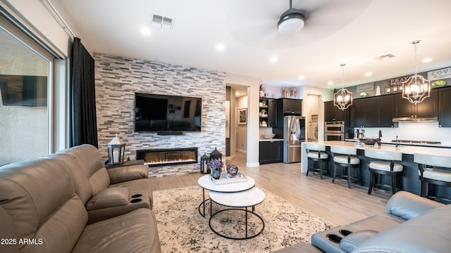 living room with light wood-type flooring, visible vents, ceiling fan, and a fireplace