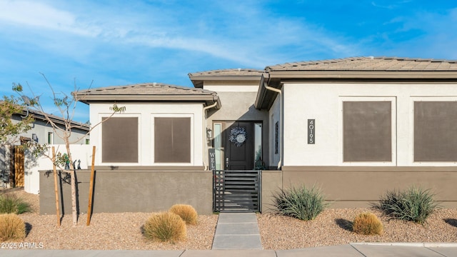 prairie-style house with a tiled roof, a fenced front yard, a gate, and stucco siding