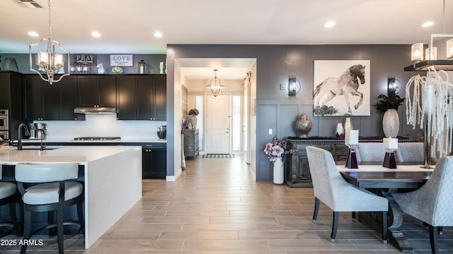 kitchen featuring under cabinet range hood, a sink, gas stovetop, light countertops, and wood tiled floor