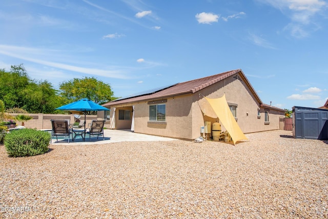 rear view of property featuring an outdoor structure, stucco siding, a storage shed, a patio, and solar panels
