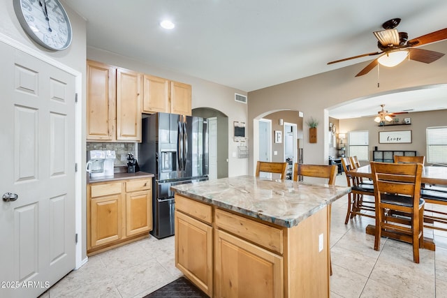 kitchen with visible vents, black fridge with ice dispenser, a center island, light brown cabinets, and backsplash