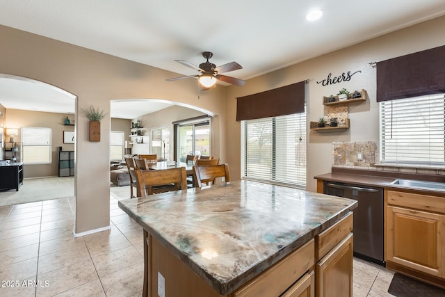 kitchen featuring arched walkways, a center island, light tile patterned floors, stainless steel dishwasher, and a ceiling fan