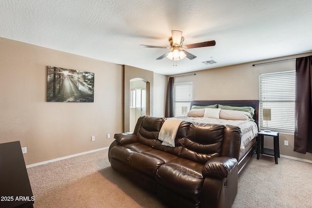 carpeted bedroom featuring baseboards, visible vents, a ceiling fan, arched walkways, and a textured ceiling