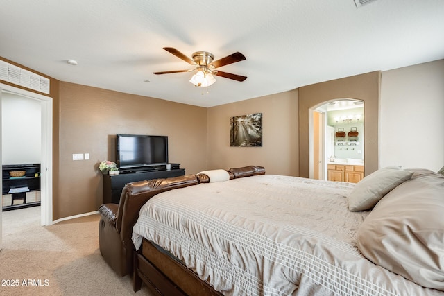 bedroom featuring arched walkways, ensuite bathroom, light carpet, a ceiling fan, and baseboards