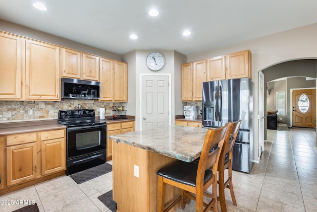 kitchen with appliances with stainless steel finishes, arched walkways, tasteful backsplash, and light brown cabinetry