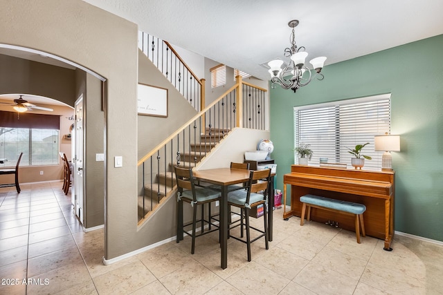 dining area with baseboards, arched walkways, stairway, tile patterned flooring, and ceiling fan with notable chandelier