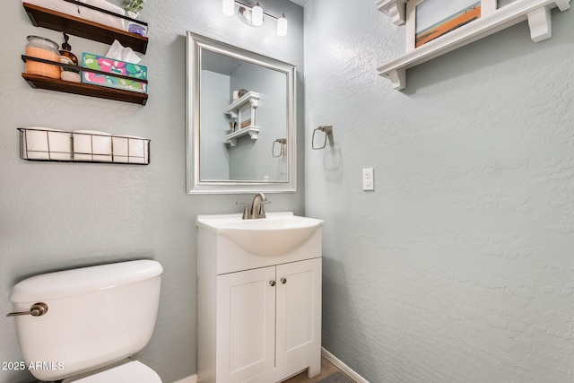 half bathroom featuring toilet, a textured wall, and vanity