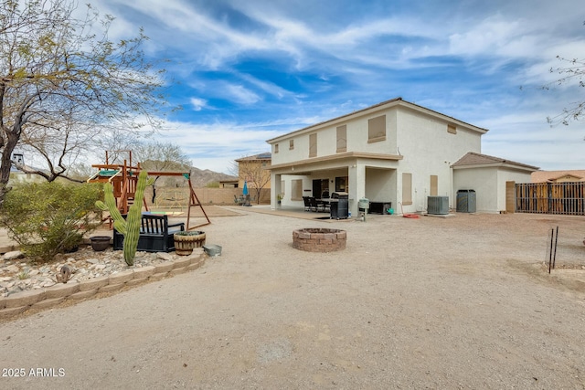 rear view of property with a playground, an outdoor fire pit, a patio area, fence, and central AC