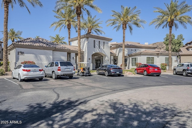 mediterranean / spanish house featuring stucco siding, a tile roof, and uncovered parking