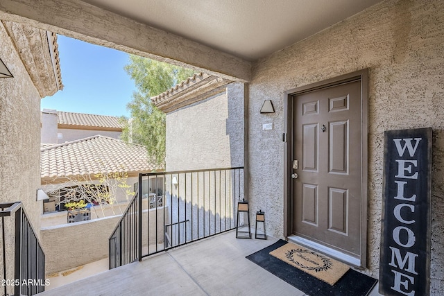 property entrance with a tiled roof, a balcony, and stucco siding