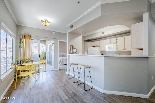 kitchen with light wood finished floors, visible vents, crown molding, and white appliances