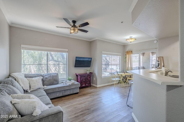 living room featuring baseboards, ornamental molding, light wood-style flooring, and a ceiling fan