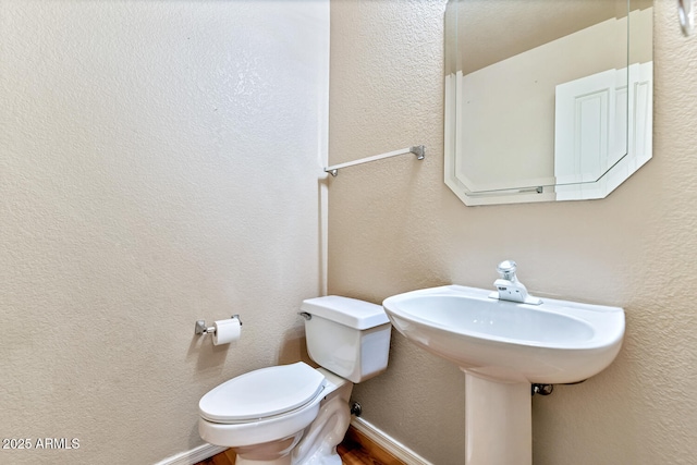 half bathroom with baseboards, a textured wall, and toilet