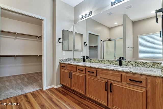 bathroom with wood finished floors, a stall shower, a sink, and visible vents