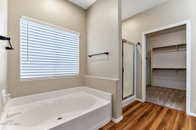 full bath featuring a shower stall, a spacious closet, a bath, and wood finished floors