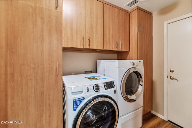 laundry area featuring light wood-type flooring, washer and dryer, cabinet space, and visible vents