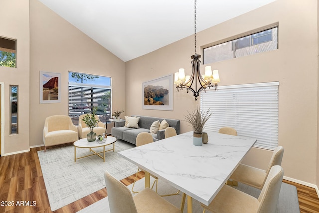 dining space featuring high vaulted ceiling, baseboards, a chandelier, and wood finished floors