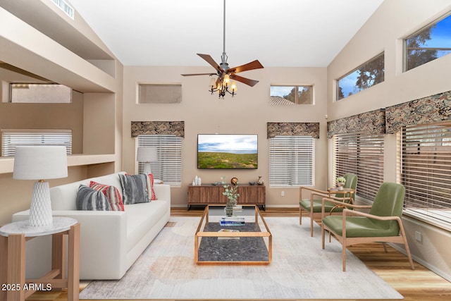 living area with visible vents, a towering ceiling, a ceiling fan, wood finished floors, and baseboards