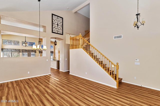 unfurnished living room featuring a chandelier, wood finished floors, arched walkways, and stairs