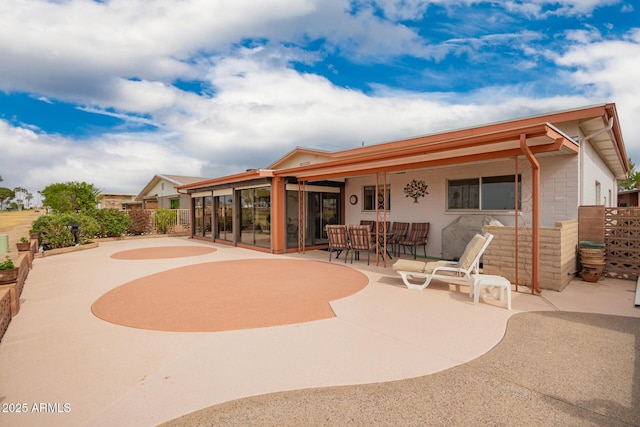 rear view of property featuring a sunroom, a patio, and fence