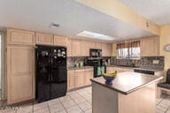 kitchen with freestanding refrigerator, a center island, light tile patterned flooring, and light brown cabinetry