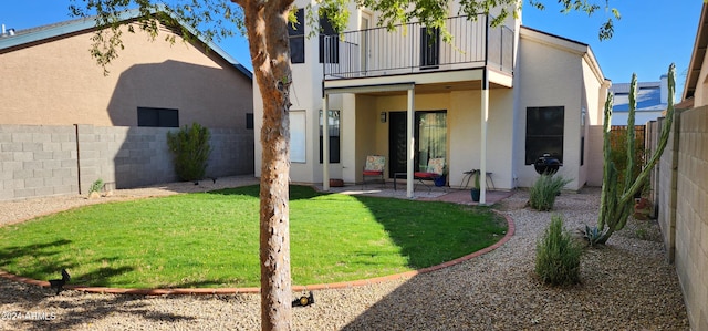 rear view of house with a lawn, a balcony, and a patio