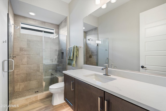 bathroom with a stall shower, vanity, toilet, and wood finished floors