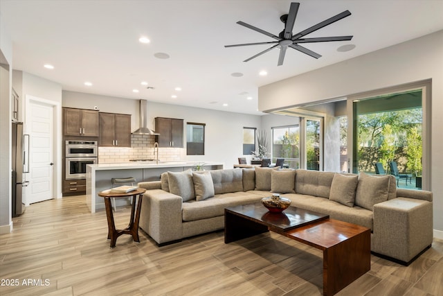 living room with light wood-type flooring, a ceiling fan, and recessed lighting